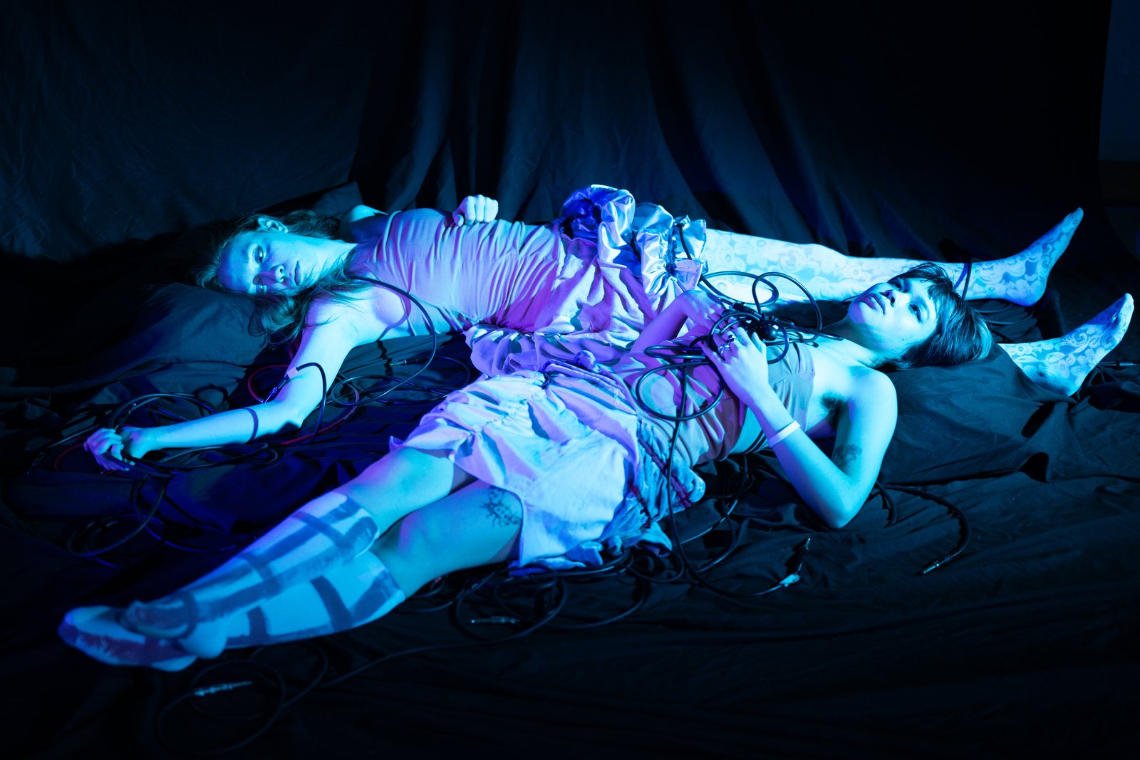 Post Apocalypse, two models reclining with cables in blue light